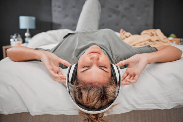 musique de sommeil, lit et femme écoutant un podcast audio avec des écouteurs dans la chambre de sa maison. fille endormie diffusant un son radio calme pour la paix, la détente et l’esprit satisfait avec wifi à la maison - relationship difficulties audio photos et images de collection