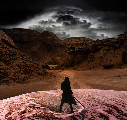 man with sword stands in water in wild canyon with storm clouds approaching