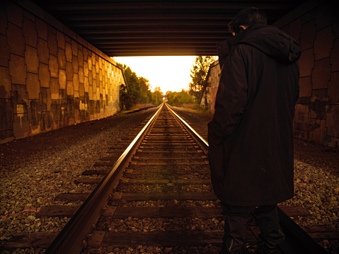 man standing on railroad tracks in a tunnel during golden hour