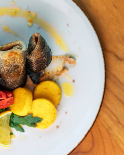 istock Fish on a white plate with potato slices, cherry tomato, lemon and arugula in a restaurant from above 1444387847