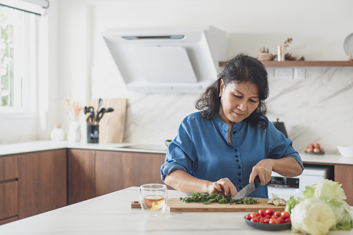 Senior asian woman prepares salad in the kitchen