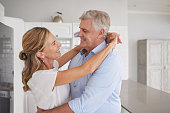 Happy senior couple, love and hug for care in joyful relationship together in the kitchen at home. Elderly man and woman smile, dancing and sharing a bonding moment of romance at the house