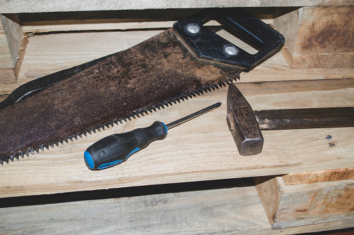 Tools for working with wood. Direct lighting on home tools. On a wooden background lies a hammer, a saw and a screwdriver.