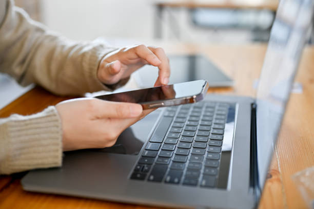 istock side view, Asian female using her smartphone at her desk, in front of the laptop computer. 1444399219