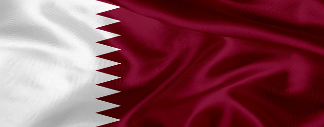Flag of Qatar blowing in the wind. \nFull page Qatari flying flag.