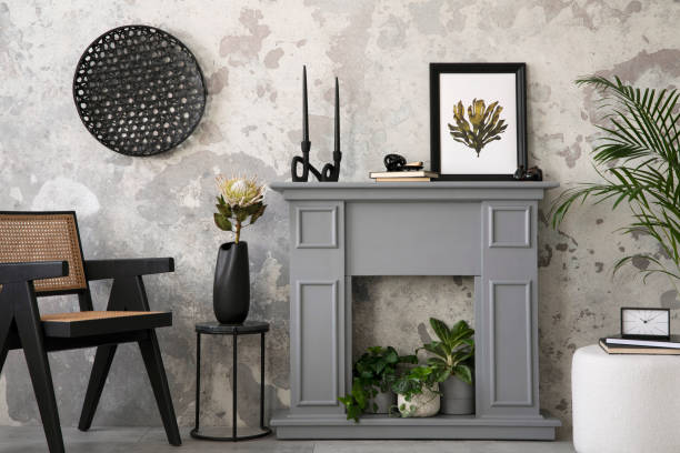 istock Creative composition of  living room interior with mock up poster frame, grey fireplace,  stylish rattan armchair, plants in flowerpots, white pouf and personal accessories. Home decor. Template. 1444401406