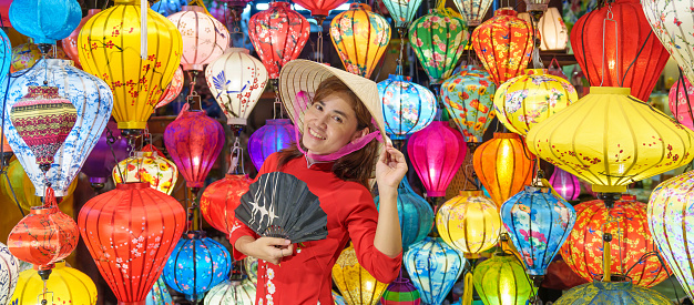 happy woman wearing Ao Dai Vietnamese dress with colorful lanterns, traveler sightseeing at Hoi An ancient town in central Vietnam.landmark for tourist attractions.Vietnam and Southeast travel concept