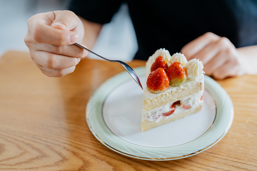 Young woman eating strawberry cake in cafe