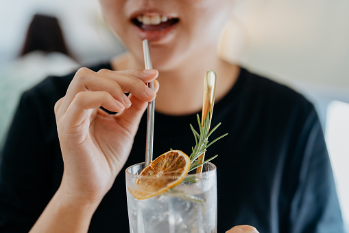 Image of an Asian Chinese woman drinking refreshing soda drink with metal straw in a cafe