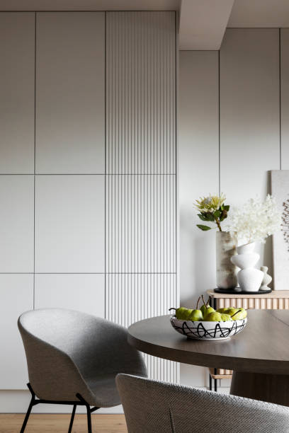 istock Interior design of stylish dining room with round table, gray chairs, modern wall, pears in patterned bowl, white vase with flowers and design personal accessories. Home decor. Template. 1444402923