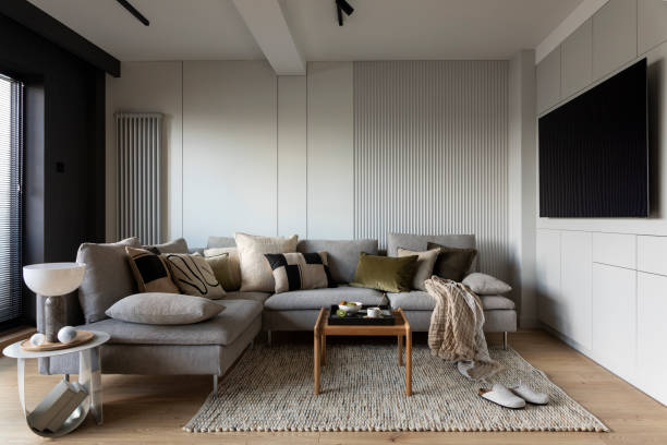 istock Creative composition of living room interior with design gray sofa, wooden coffee table, stylish carpet, beige side table, pillows, personal accessories and big tv. Stylish home decor. Template. 1444403148