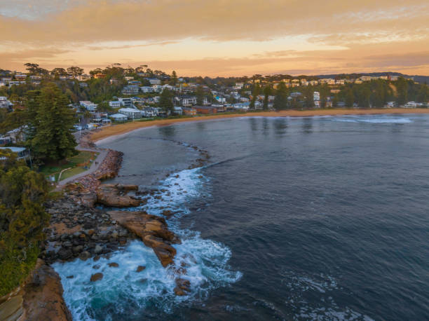 Sunrise over the ocean with rocks and coastal suburb Aerial sunrise at the seaside with rocks and gentle surf at Avoca Beach on the Central Coast, NSW, Australia. avoca beach photos stock pictures, royalty-free photos & images