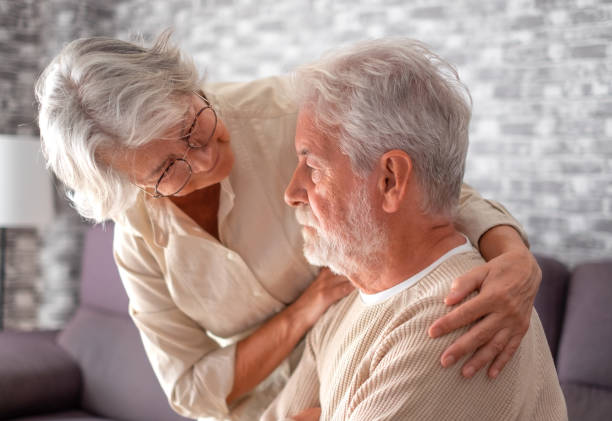 old worried senior woman comforting her depressed, mental ill husband, unhappy elderly man at home need medical help. ourmindsmatter - cuidado com o corpo imagens e fotografias de stock