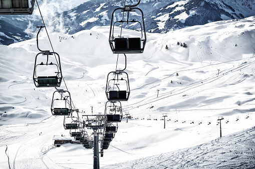 Big ski lift with chairs over the snowy ski track on top of the Alps mountains. Extreme winter sports theme
