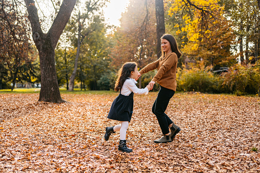 Young mother and daughter dancing in the park in autumn.