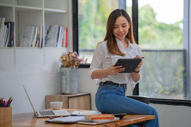istock Asian businesswoman sitting on an office desk and using a tablet. 1444413404