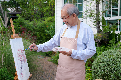 Senior painting picture, old man drawing in garden. Senior holding color paint drawing on white paper. Elderly activities on free time. happy elderly. life after retirement concept.