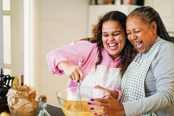 African mother and daughter having fun preparing fruit cake at home - Soft focus on senior woman face stock photo