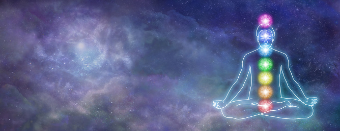 Male outline lotus position with 7 rainbow coloured energy centres centrally placed against a deep space nebula night sky background and copy space