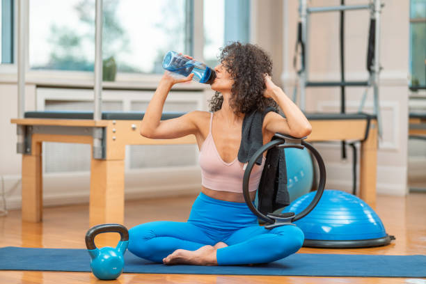 istock Curly haired woman drinks water from a plastic bottle after exercise in a pilates studio 1444429100