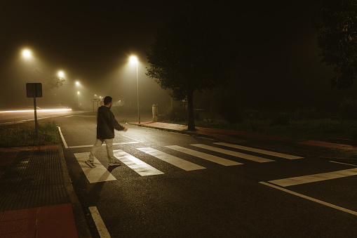 Sad man alone walking along the alley in night foggy park. Front view.