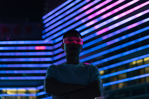 Man using smart glasses to experience metaverse at night against neon light background