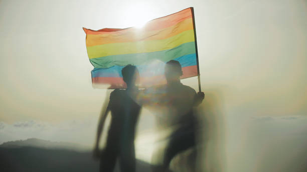 Two gay man celebrating LGBT pride month. Holding hands and waving rainbow flag stock photo