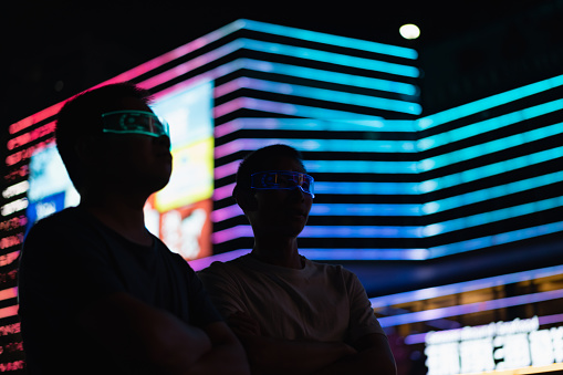 Two men experience a virtual reality game using glowing smart glasses at night on a neon light background