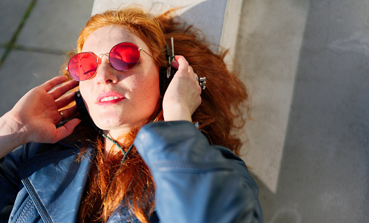 Portrait of beautiful young woman with red sunglasses and headphones. She is out and about in the city.