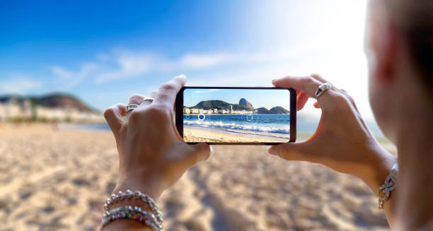 donna nella spiaggia di copacabana che scatta una foto con il suo telefono cellulare. rio de janeiro, brasile. - take picture foto e immagini stock
