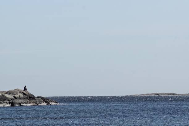 Unrecognizable person sitting on cliff at sea