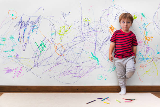 méfait d’enfant. garçon avec un visage distrait parce qu’il a dessiné tout le mur. - espièglerie photos et images de collection