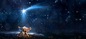 istock Nativity Scene - Birth Of Jesus Christ With Manger In Snowy Night And Starry Sky - Abstract Defocused Background 1444449094