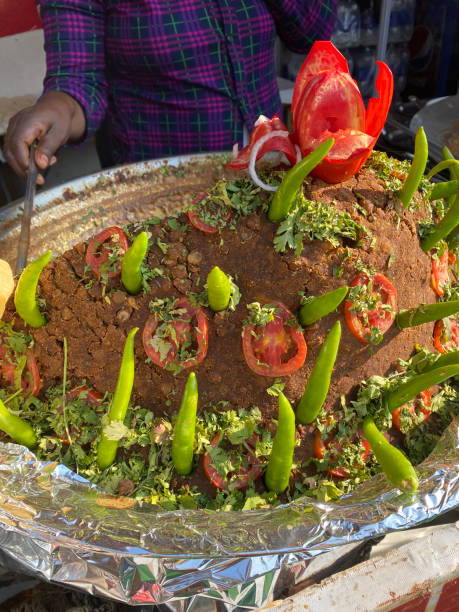 Stock photo showing popular Indian street food Punjabi chole a traditional Indian chickpea curry sold by street food vendors as breakfast on streets or market stalls in India. Unhygenic food, Delhi belly concept. imagen en primer plano de una persona irreconocible que sirve comida callejera de punjabi chole (curry de garbanzos) cubierto con chiles verdes y tomates en rodajas de una sartén grande, comida sabrosa tradicional india en el puesto del mercado, vista ele
