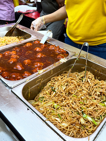 Stock photo showing close-up view of some traditional Indian street food being sold at a market stall. A large metal serving tray of spicy Singapore noodles, with chillies, bell peppers and onions. The noodles were cooked outside for al fresco dining, on a gas cooking stove hob for hungry shoppers and passersby.