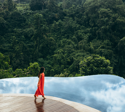 Beautiful woman walking on the edge of an infinity pool in a jungle during sunrise