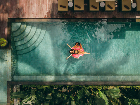 Aerial view of couple enjoying in resort pool. Young woman lying on inflatable ring with man in resort swimming pool.