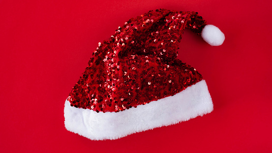 Close-up of a red shiny santa claus hat on a red background,top view, flat lay, copy space. Decor concept for christmas or new year party. Christmas suit.