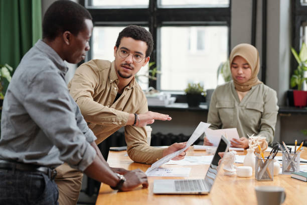 istock Young confident businessman with document making presentation to colleagues 1444470632