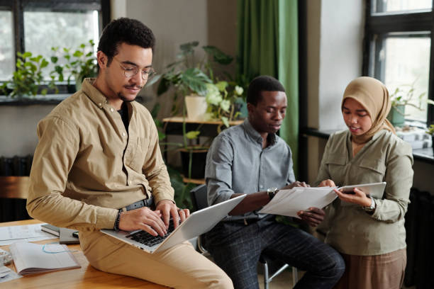 istock Young broker with laptop on his knees sitting on desk and networking 1444470673