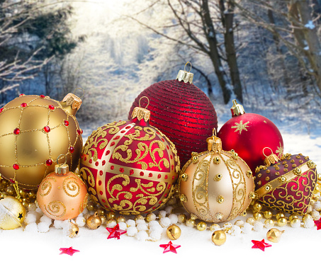 Heap of christmas balls in gold and red colors and gift box in snow in winter forest