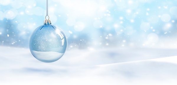 Transparent Christmas ball hanging in front of blurred snow background