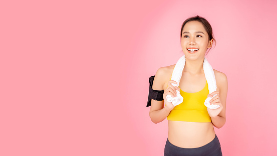 Smiling sport young asian woman looking up to copy space Happy girl hanging towel around neck with smile face and happiness isolated on pink background Copy space Health care and Sport concept