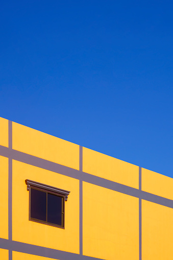 Street minimal architecture background. Glass window on colorful yellow and purple building wall against blue clear sky in vertical frame