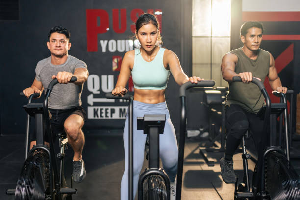 gruppo di giovani atleti che fanno esercizio insieme in palestra fitness. attraenti esercizi di allenamento per sportivi attivi e donne insieme pedalando su una macchina da bici per la salute e il benessere nello stadio. - spinning health club instructor gym foto e immagini stock