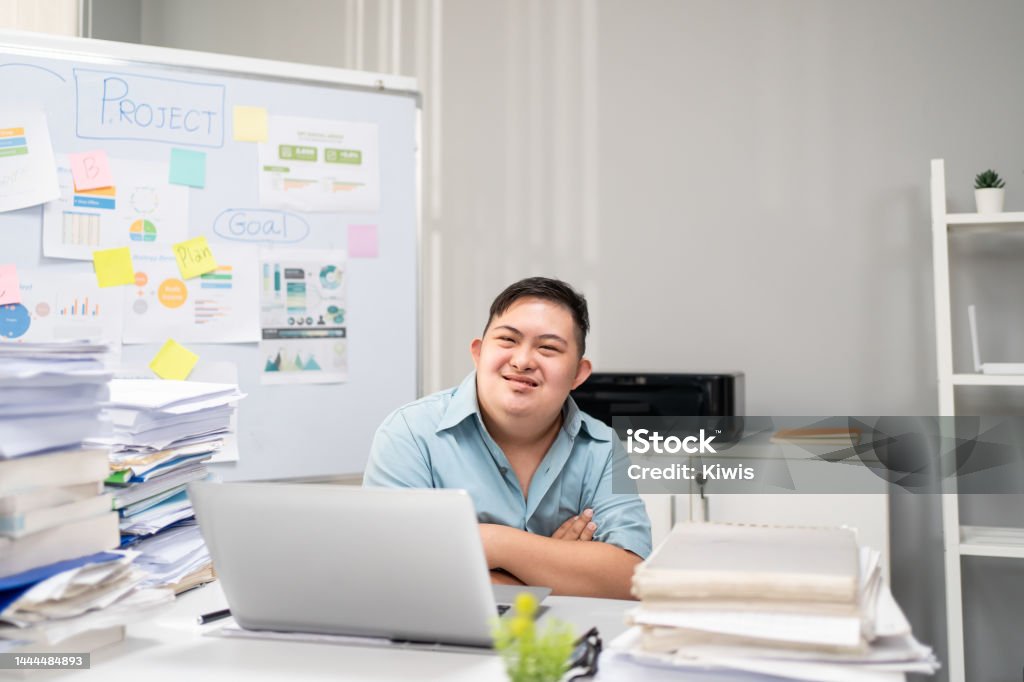 Portrait of Asian young businessman with down syndrome work in office. Employee man worker people sitting on table, planning project alone in corporate workplace then smiling, looking at camera. Autism Stock Photo