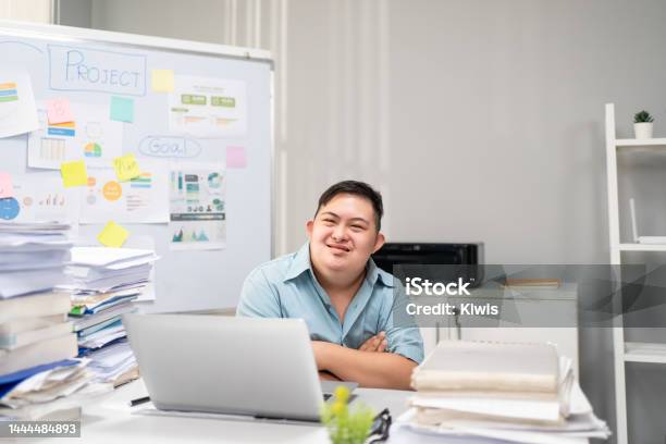 Portrait Of Asian Young Businessman With Down Syndrome Work In Office Employee Man Worker People Sitting On Table Planning Project Alone In Corporate Workplace Then Smiling Looking At Camera Stock Photo - Download Image Now