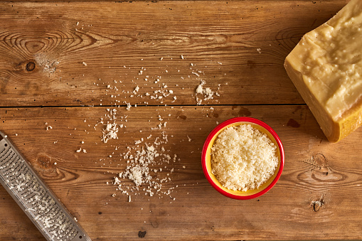 Overhead view of finely grated cheese in a bowl with block and stainless steel grater with cheese sprinkled on wooden table