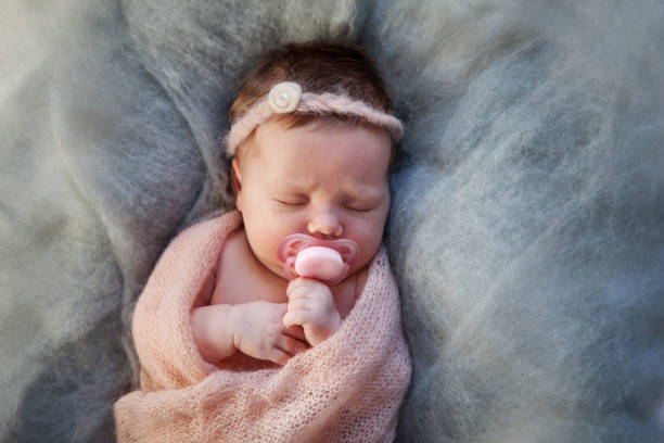 retrato de un bebé recién nacido dormido con maniquí, envuelto en una cálida manta de punto. el niño chupa el pezón del chupete - niñas bebés fotografías e imágenes de stock