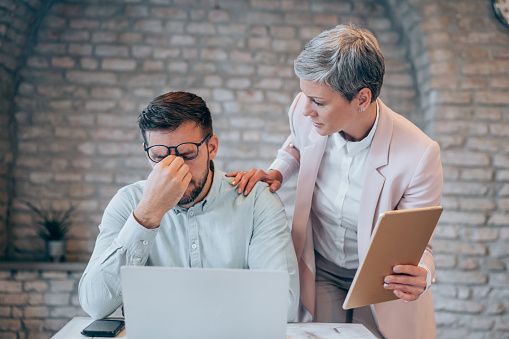 Shot of a young man looking annoyed as his colleague speaks to him. Stressed businessman having headache while working on laptop in the office.